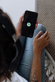 A person listening to music with headphones and smartphone, displaying Spotify logo.