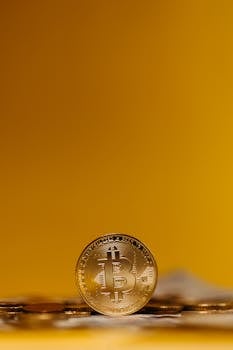 Close-up of a Bitcoin coin standing upright on a blurred yellow background, symbolizing digital finance.