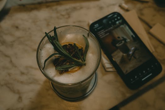 Close-up view of a matcha latte with garnish alongside a smartphone on a marble table, indoors.