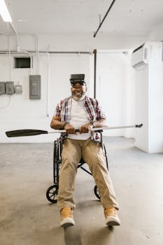 A man in a wheelchair wearing a VR headset and holding a paddle in an industrial setting.