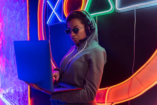 Young woman in a hoodie using a laptop, surrounded by neon lights, creating a futuristic vibe.