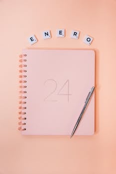 Minimalist flat lay of a pink notebook, pen, and ENERO tiles on a peach background.