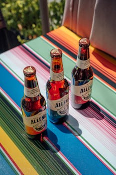 Three Allende beer bottles on a vibrant Mexican tablecloth in sunlight.